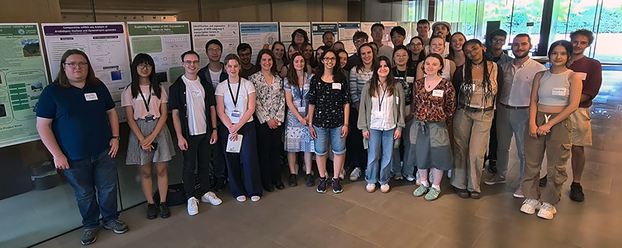 Plant Biology summer students standing together in front of poster boards in Sainsbury Laboratory atrium