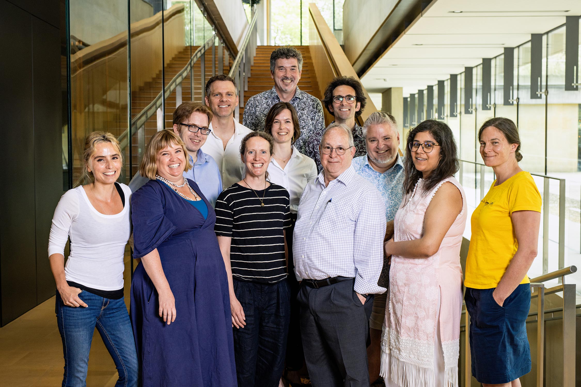Sainsbury Laboratory Group Leaders Group photo with all SLCU Group Leaders standing at base of stairs in SLCU building with background lokking out to courtyard