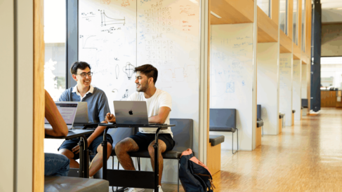 Two researechers talking while sitting in a window study box with a laptop each.