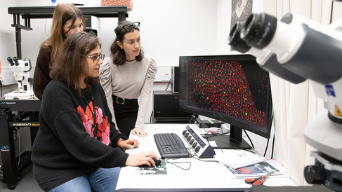 Three women scientists looking at a leaf imaged under a confocal microscope.