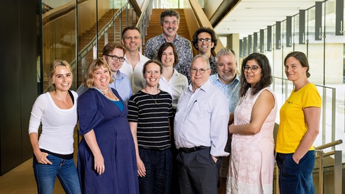 Group photo with all SLCU Group Leaders standing at base of stairs in SLCU building with background lokking out to courtyard