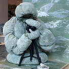 The puffer jacket with the flavonoid wool covering on a model holding a camera as on display. The material is a soft green colour.