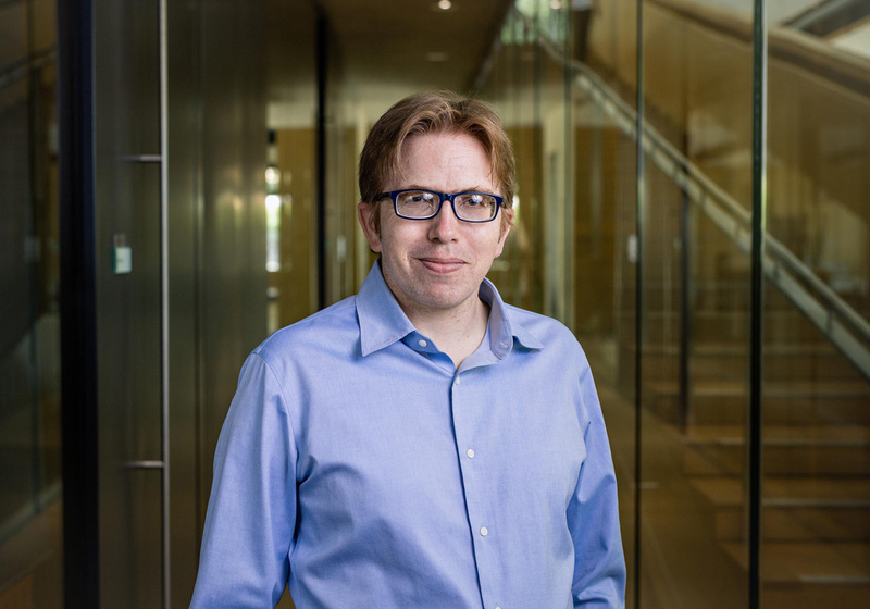 Professor James Locke standing at foot of internal staircase with glass wall in background inside the Sainsbury Laboratory building