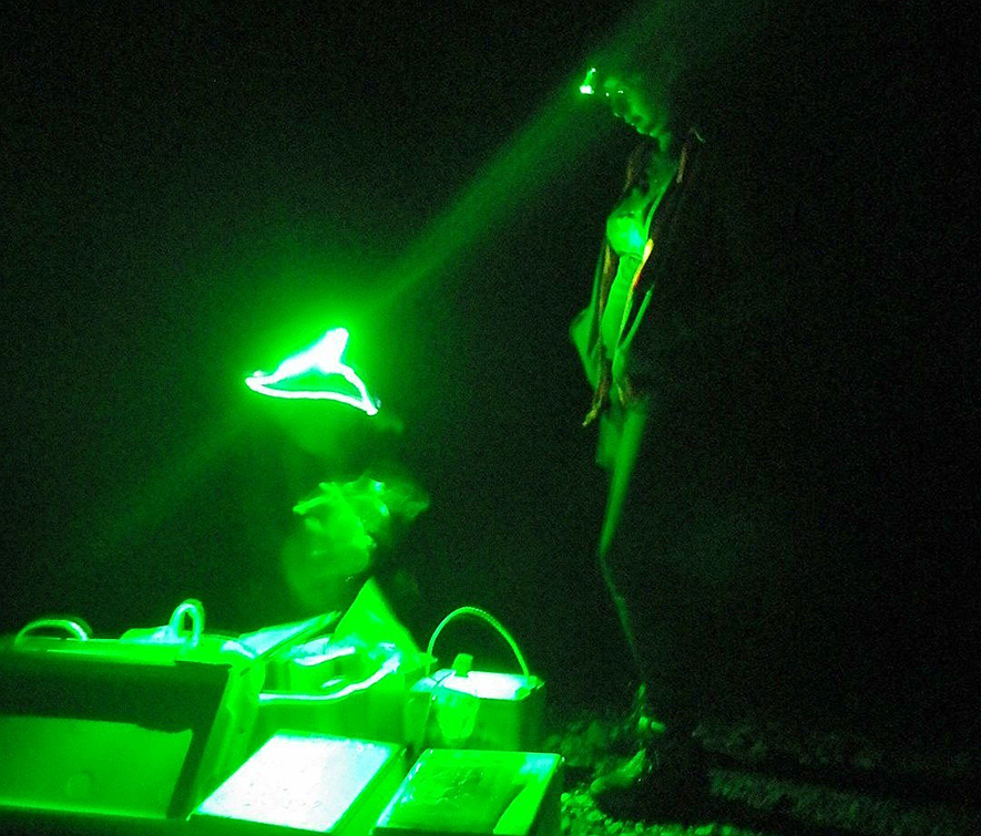 Dora Cano-Ramirez working under green light at night in field experiments in Japan. Dora Cano-Ramirez working under green light at night in field experiments in Japan. Dora wears a green headlamp to illuminate the scientific equipment boxes on the ground.