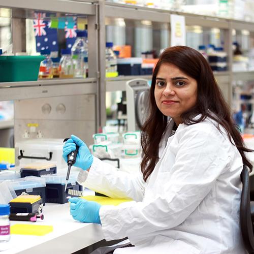 Mahwish Ejaz sitting on a stool working at her lab bench at the Sainsbury Laboratory